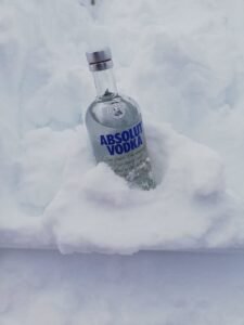 A bottle of premium vodka nestled in fresh snow, highlighting its coldness and purity.