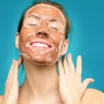 Close-up of a smiling woman with a clay facial mask, conveying relaxation and skincare routine. beauty