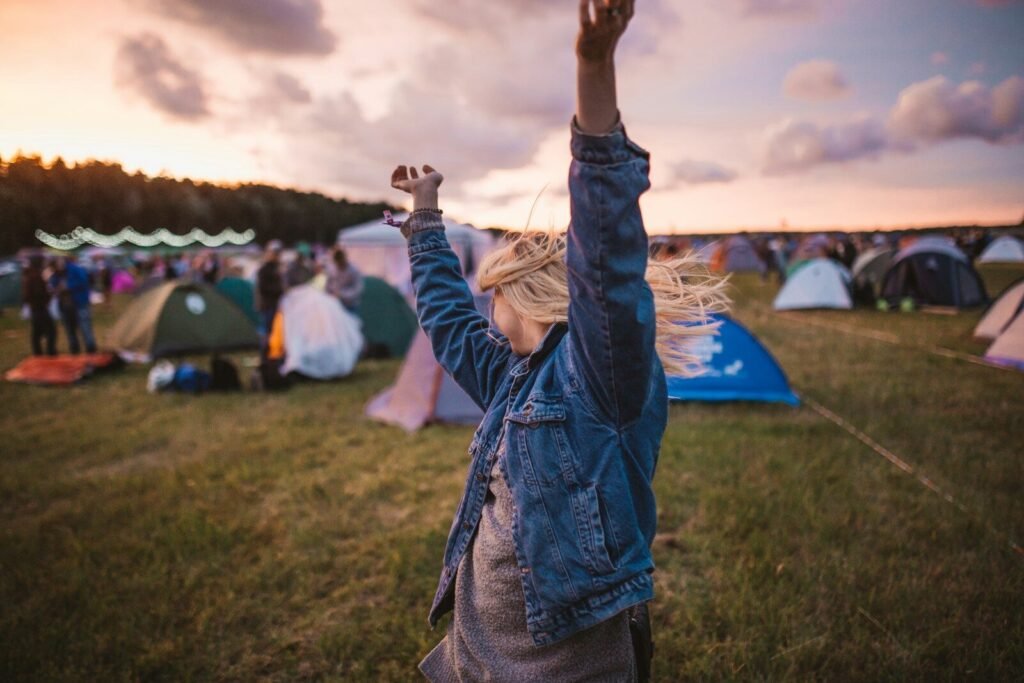 a woman raising her arms in the air in front of tents, music festival, beach