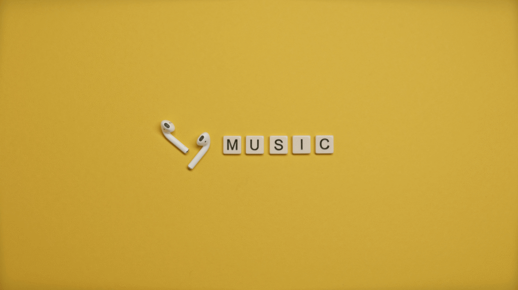 Minimalist image of AirPods and music-themed letter tiles on a vibrant yellow background. plays