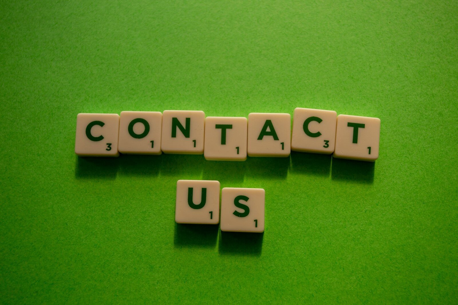 Contact US 1 white and black dice on green textile, contact us