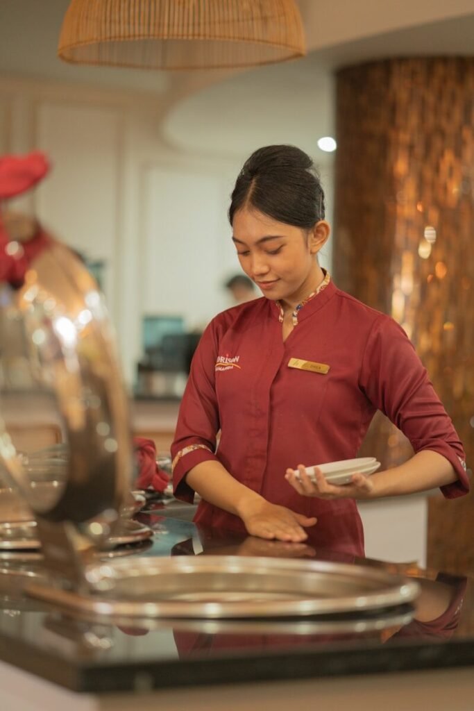 A server in a maroon uniform arranging plates, workers