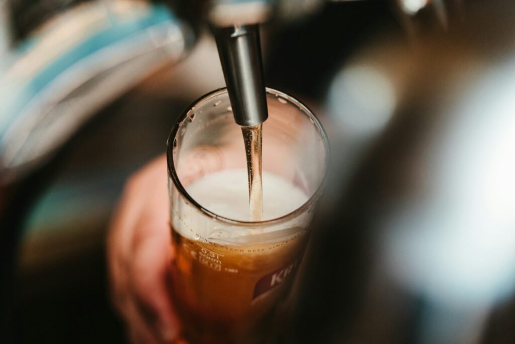 person filling clear glass with liquid, beer