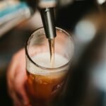 person filling clear glass with liquid, beer